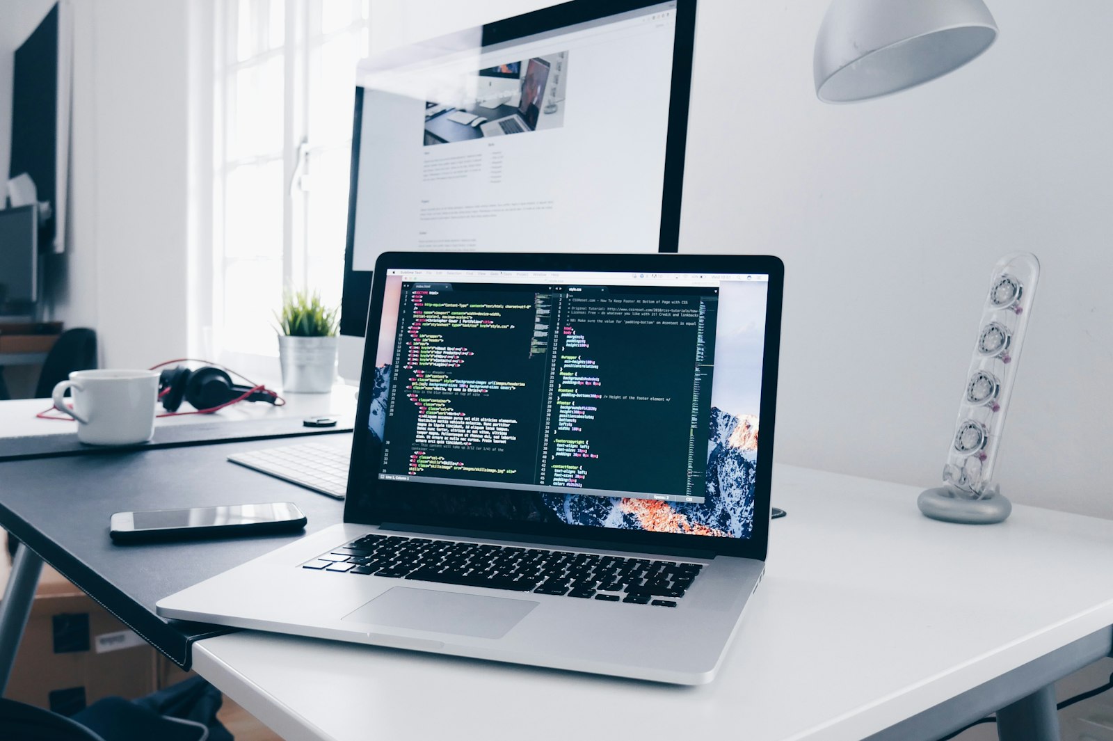 A desk with a laptop of code and a website on the monitor